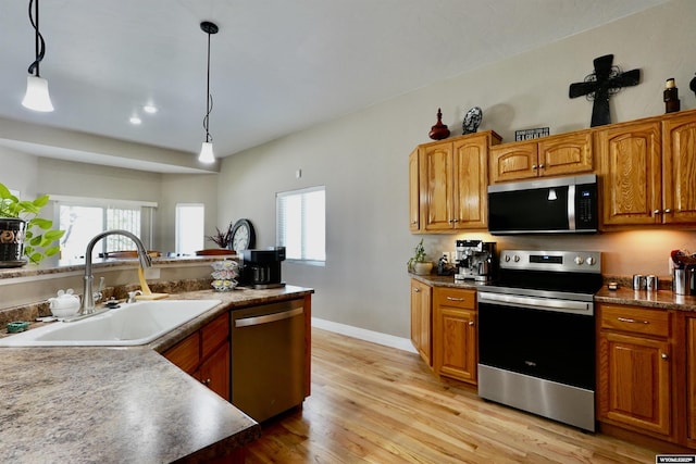kitchen with light wood-type flooring, brown cabinets, a sink, decorative light fixtures, and stainless steel appliances