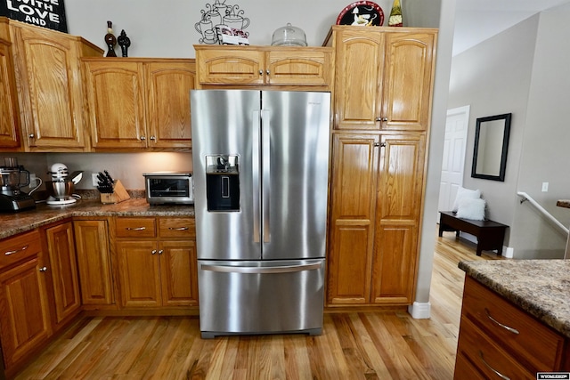 kitchen featuring brown cabinetry, a toaster, dark stone countertops, stainless steel fridge, and light wood-style flooring