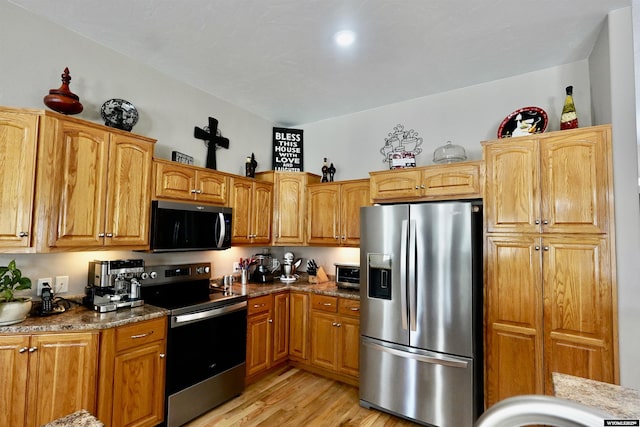 kitchen featuring appliances with stainless steel finishes, dark stone countertops, brown cabinetry, and light wood-type flooring