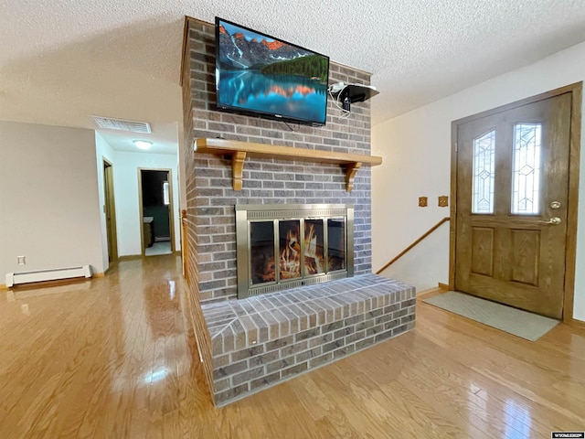 unfurnished living room featuring baseboard heating, a fireplace, a textured ceiling, baseboards, and wood finished floors