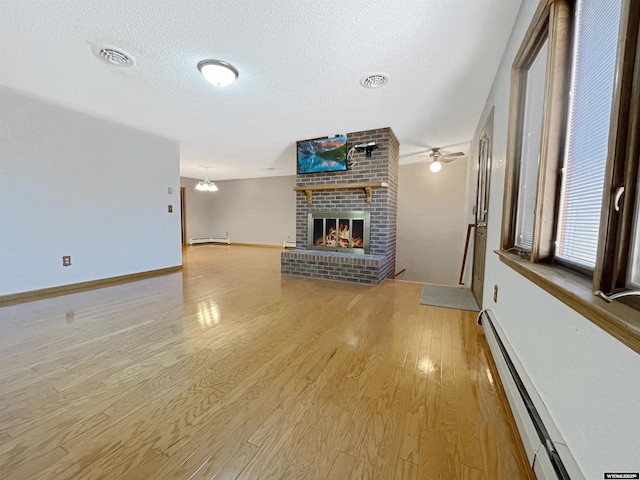 unfurnished living room featuring light wood-style floors, a textured ceiling, a baseboard heating unit, and a brick fireplace