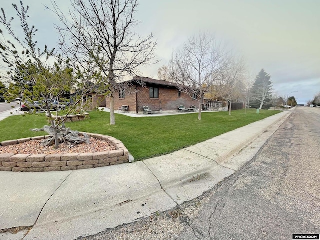 view of front facade featuring brick siding, a patio area, and a front lawn