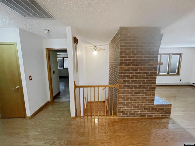 hallway with visible vents, wood finished floors, baseboards, a textured ceiling, and an upstairs landing