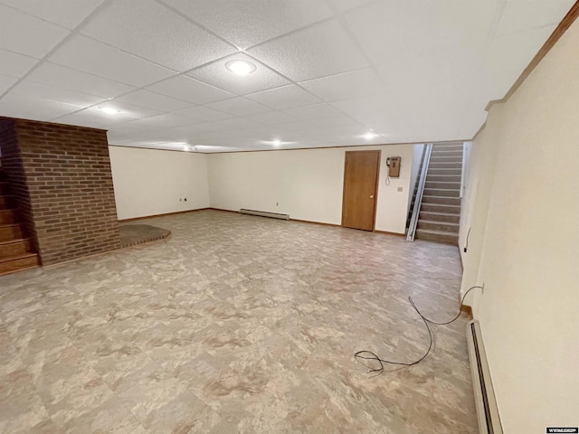 finished basement with a paneled ceiling, baseboard heating, baseboards, a baseboard radiator, and stairs
