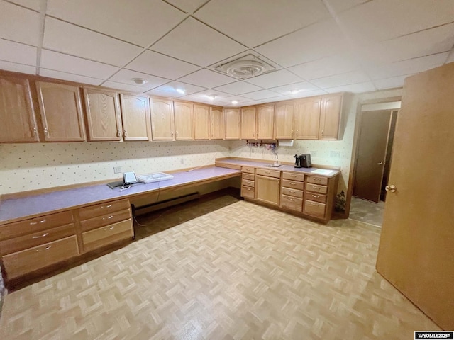 kitchen with a sink, built in desk, light brown cabinets, light countertops, and a drop ceiling