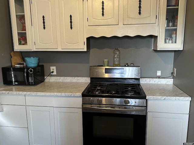 kitchen featuring black microwave, light countertops, stainless steel gas range, glass insert cabinets, and white cabinetry