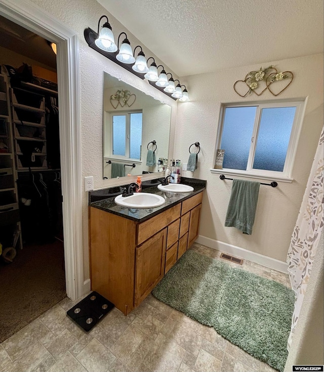 999 Eagle Dr, Douglas, WY 82633 - full bath with double vanity, a textured ceiling, a walk in closet, a textured wall, and stone finish floors
