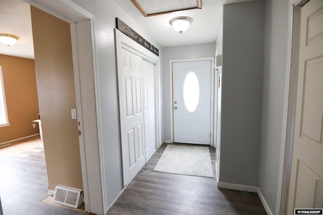 doorway to outside with baseboards, a textured ceiling, visible vents, and wood finished floors