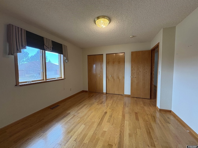 2327 Crestview Dr, Torrington, WY 82240 - unfurnished bedroom with visible vents, two closets, baseboards, light wood-type flooring, and a textured ceiling