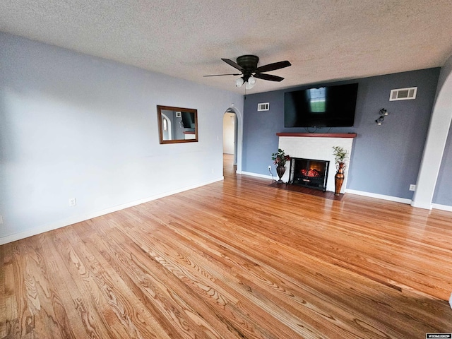 unfurnished living room with visible vents, a fireplace with flush hearth, ceiling fan, a textured ceiling, and arched walkways