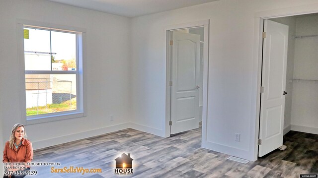 unfurnished bedroom with baseboards, a spacious closet, and wood finished floors