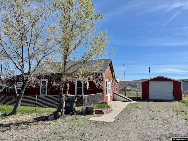 view of property exterior featuring a garage, dirt driveway, fence, and an outbuilding