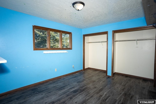 unfurnished bedroom featuring baseboards, two closets, a textured ceiling, and dark wood-type flooring