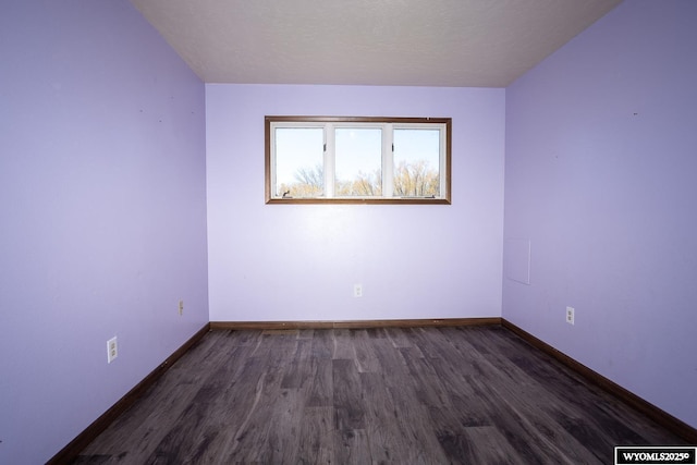 unfurnished room with baseboards and dark wood-type flooring