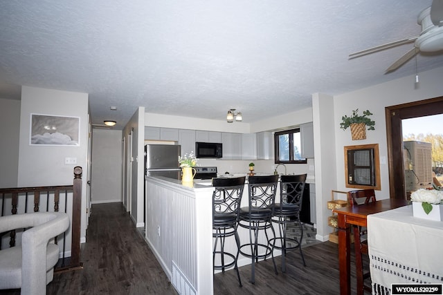 kitchen featuring stainless steel electric stove, black microwave, refrigerator, and dark wood-style floors