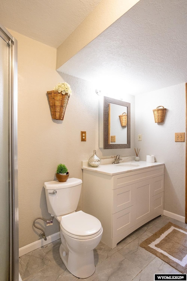 bathroom with vanity, a textured ceiling, baseboards, and toilet