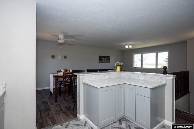 kitchen featuring a ceiling fan, a textured ceiling, light stone countertops, light wood-type flooring, and baseboards