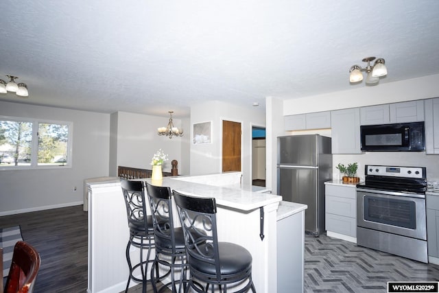 kitchen featuring a breakfast bar, baseboards, a chandelier, gray cabinetry, and stainless steel appliances