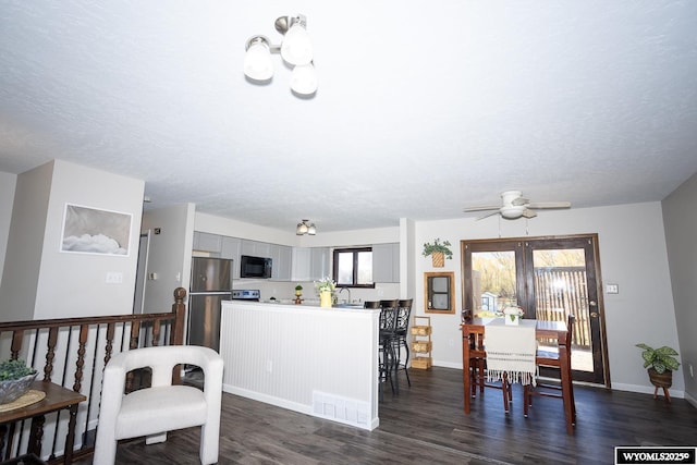 kitchen with black microwave, gray cabinets, freestanding refrigerator, visible vents, and dark wood-style floors