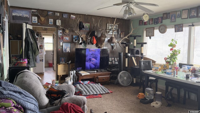 living room featuring carpet floors, a ceiling fan, wood walls, and a healthy amount of sunlight
