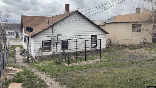back of house featuring fence, a chimney, a yard, and a shingled roof