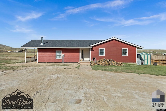 ranch-style house featuring a storage unit, fence, a shingled roof, and an outbuilding