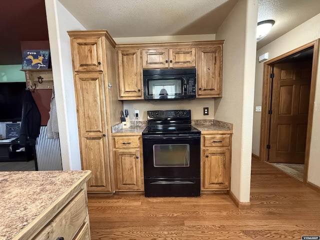 kitchen with light wood-type flooring, a textured ceiling, light countertops, and black appliances