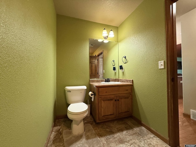 bathroom featuring vanity, toilet, and a textured wall