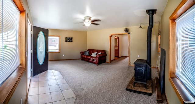 living room featuring a wood stove, light colored carpet, ceiling fan, light tile patterned floors, and baseboards