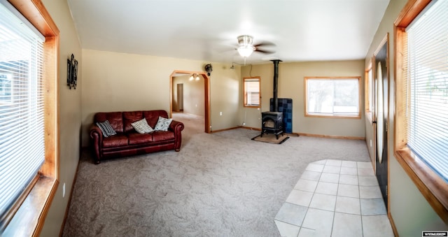living room featuring light carpet, a wood stove, a ceiling fan, and baseboards
