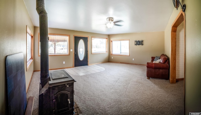 entryway featuring a wood stove, a ceiling fan, carpet, and baseboards