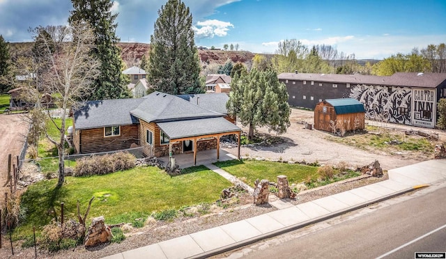 view of front of home with a storage unit, a patio area, log siding, an outdoor structure, and roof with shingles