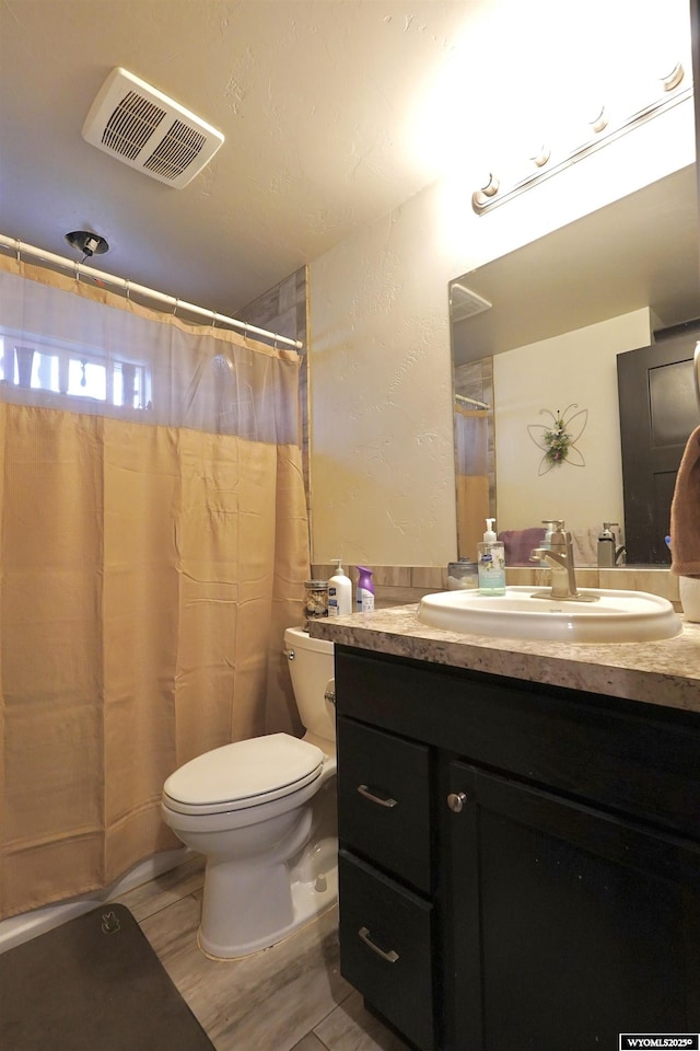 full bath featuring toilet, vanity, curtained shower, visible vents, and a textured wall