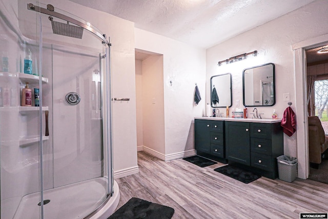 bathroom with a sink, double vanity, a shower stall, and wood finished floors