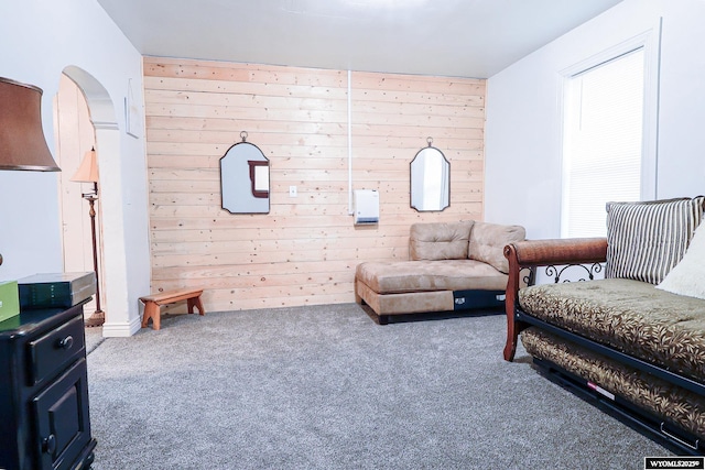carpeted living area with wood walls and arched walkways
