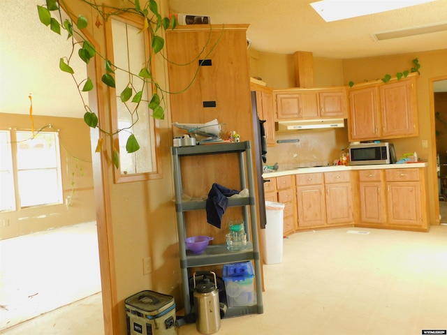 479 Hoskins Ln, Rock Springs, WY 82901 - kitchen with light brown cabinetry, under cabinet range hood, stainless steel microwave, light countertops, and a skylight
