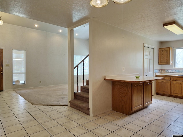 kitchen with a textured ceiling, light countertops, light tile patterned floors, and brown cabinets