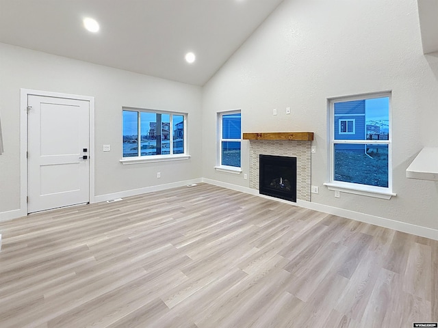 unfurnished living room with high vaulted ceiling, light wood-type flooring, baseboards, a fireplace, and recessed lighting
