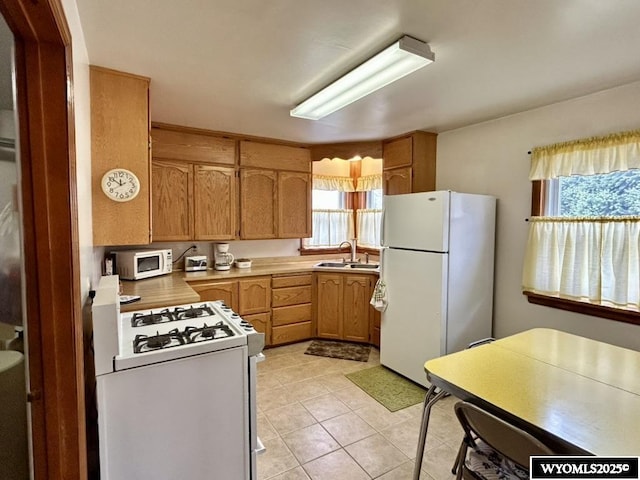 kitchen with white appliances, a sink, light tile patterned floors, light countertops, and brown cabinets
