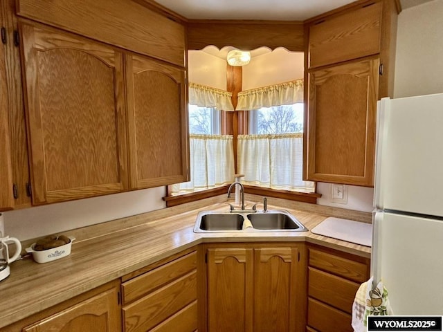 kitchen featuring freestanding refrigerator, a sink, light countertops, and brown cabinets