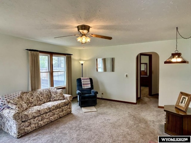 carpeted living room with arched walkways, a ceiling fan, a textured ceiling, and baseboards