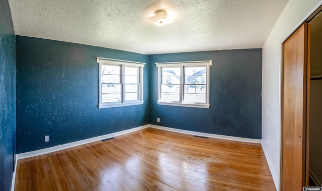 empty room featuring wood finished floors, a textured ceiling, baseboards, and a textured wall