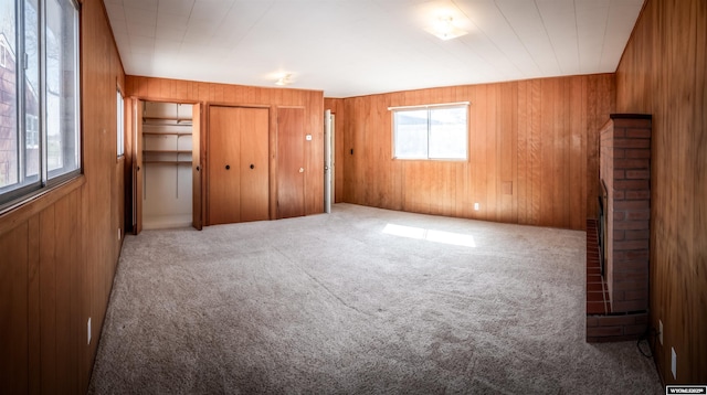 unfurnished bedroom with carpet flooring, wood walls, and a brick fireplace
