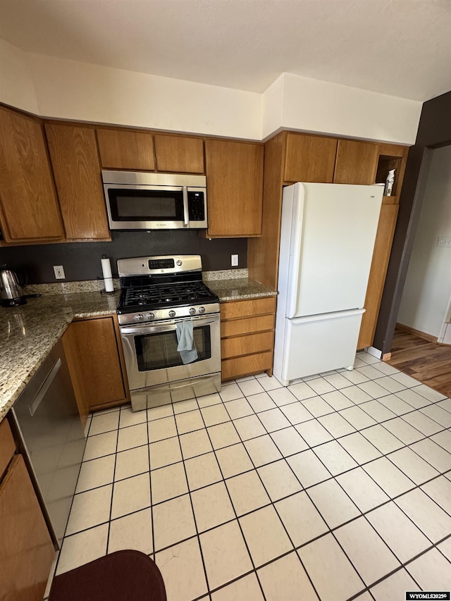 191 Lester Dr, Rock Springs, WY 82901 - kitchen featuring stainless steel appliances, brown cabinetry, light tile patterned floors, and dark stone countertops