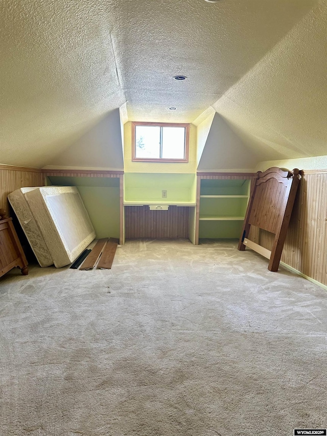 bonus room featuring a textured ceiling, carpet flooring, lofted ceiling, and wooden walls