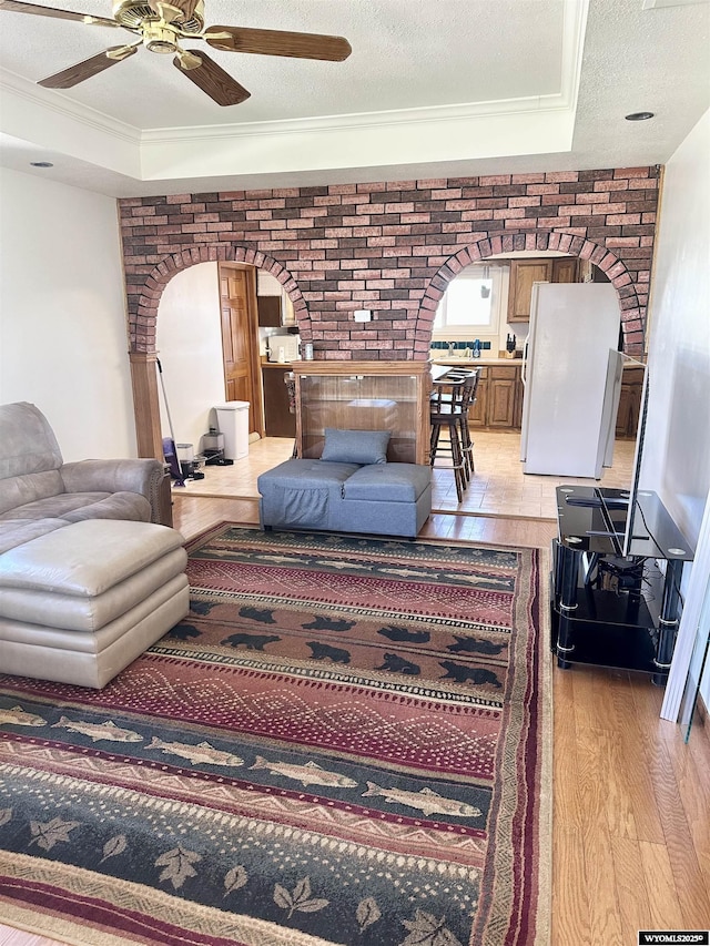 living room with arched walkways, light wood-type flooring, ceiling fan, a textured ceiling, and ornamental molding