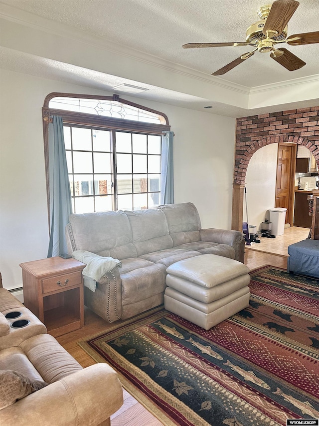 living area featuring crown molding, wood finished floors, a ceiling fan, arched walkways, and a textured ceiling