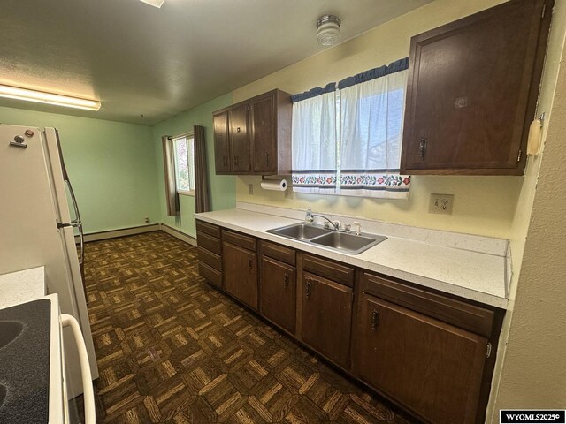 kitchen featuring stove, a sink, dark brown cabinets, light countertops, and baseboard heating