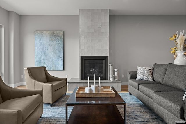 living area with dark wood-type flooring, a tiled fireplace, and baseboards
