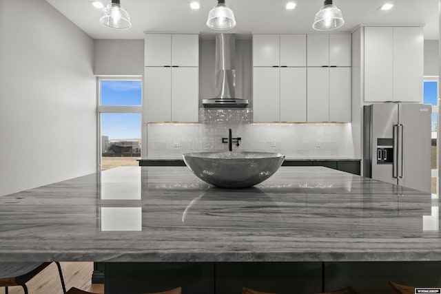kitchen featuring wall chimney range hood, modern cabinets, high quality fridge, and backsplash